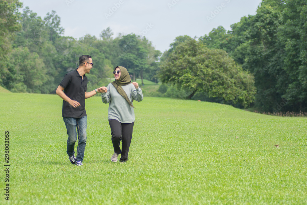 Young playful young muslim Asian couple running together hand by hand on natural background Young playful young muslim Asian couple running together hand by hand on natural background