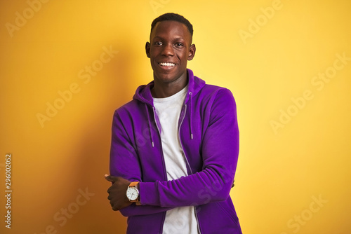 African american man wearing purple sweatshirt standing over isolated yellow background happy face smiling with crossed arms looking at the camera. Positive person.