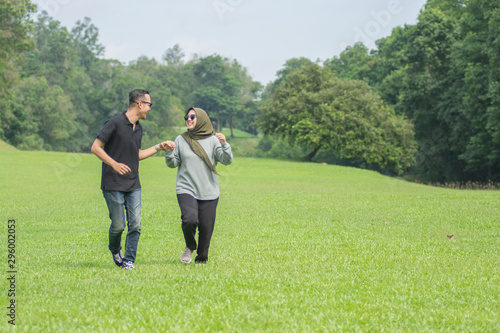 Young playful young muslim Asian couple running together hand by hand on natural background