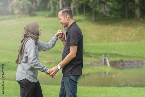 Asian young Muslim couples are enjoying being together by dancing in the open green area © SVRSLYIMAGES