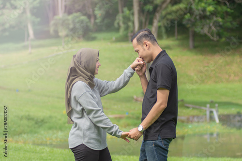 Asian young Muslim couples are enjoying being together by dancing in the open green area © SVRSLYIMAGES