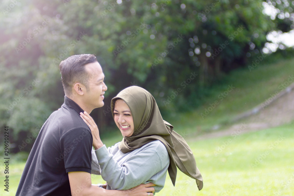 Outdoors photo, beautiful, young muslim couple, hugging and kissing and being affectionate with each other. nature in the background.