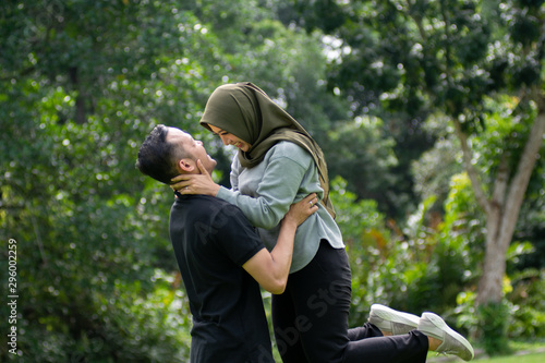 Outdoors photo, beautiful, young muslim couple, hugging and kissing and being affectionate with each other. nature in the background.