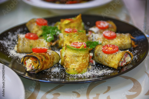Vegetarian rolls with squash, tomato, cheese and greenery on black plate.