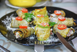 Vegetarian rolls with squash, tomato, cheese and greenery on black plate.