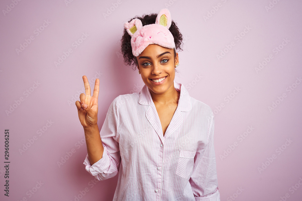 Young african american woman wearing pajama and mask over isolated pink background showing and pointing up with fingers number two while smiling confident and happy. Young african american woman wearing pajama and mask over isolated pink background showing and pointing up with fingers number two while smiling confident and happy.