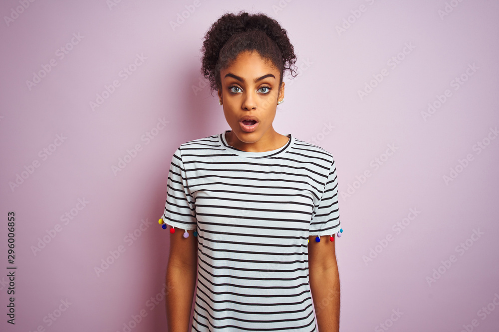 African american woman wearing navy striped t-shirt standing over isolated pink background afraid and shocked with surprise expression, fear and excited face. African american woman wearing navy striped t-shirt standing over isolated pink background afraid and shocked with surprise expression, fear and excited face.