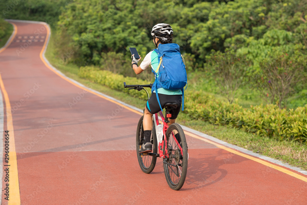 Riding on park bike path,using smartphone while riding bike on sunny day Riding on park bike path,using smartphone while riding bike on sunny day