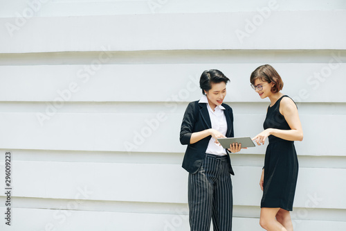 Smiling young female colleagues discussing report on tablet computer when standing outdoors