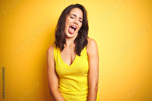 Young beautiful woman wearing t-shirt standing over yellow isolated background sticking tongue out happy with funny expression. Emotion concept.