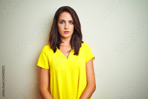 Young beautiful woman wearing yellow t-shirt standing over white isolated background with serious expression on face. Simple and natural looking at the camera.