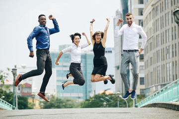 Happy excited multi-ethnic business people jumping in the air when standing on city road