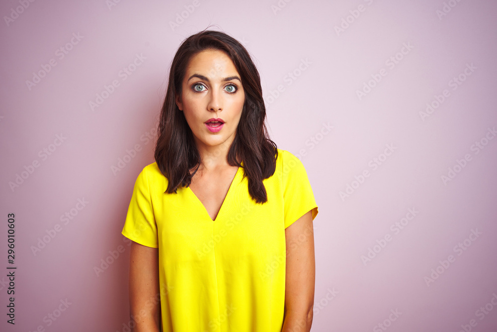 Young beautiful woman wearing yellow t-shirt standing over pink isolated background afraid and shocked with surprise expression, fear and excited face. Young beautiful woman wearing yellow t-shirt standing over pink isolated background afraid and shocked with surprise expression, fear and excited face.