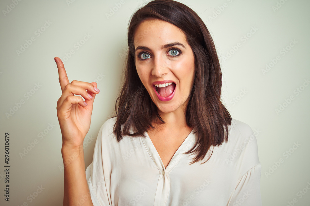 Young beautiful woman wearing casual shirt standing over white isolated background with a big smile on face, pointing with hand and finger to the side looking at the camera. Young beautiful woman wearing casual shirt standing over white isolated background with a big smile on face, pointing with hand and finger to the side looking at the camera.