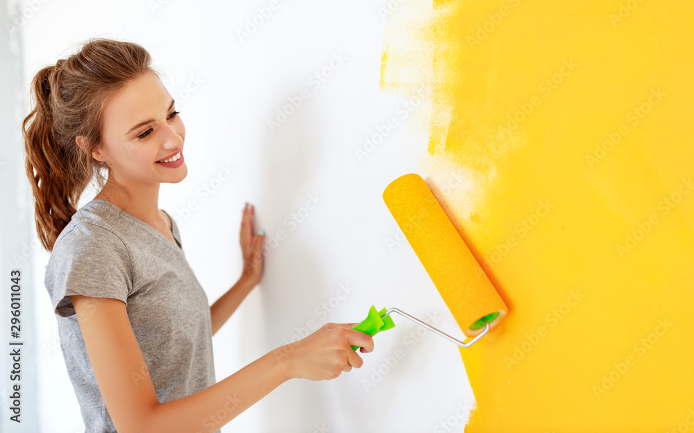 Repair in apartment. Happy young woman paints wall - obrazy, fototapety, plakaty 