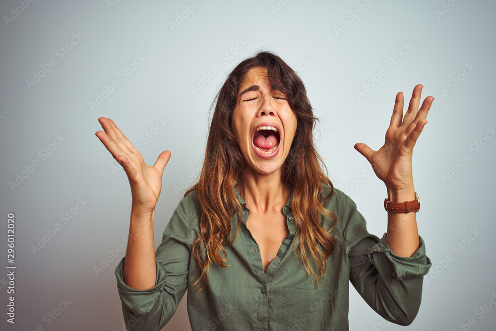 Young beautiful woman wearing green shirt standing over grey isolated background celebrating mad and crazy for success with arms raised and closed eyes screaming excited. Winner concept Young beautiful woman wearing green shirt standing over grey isolated background celebrating mad and crazy for success with arms raised and closed eyes screaming excited. Winner concept