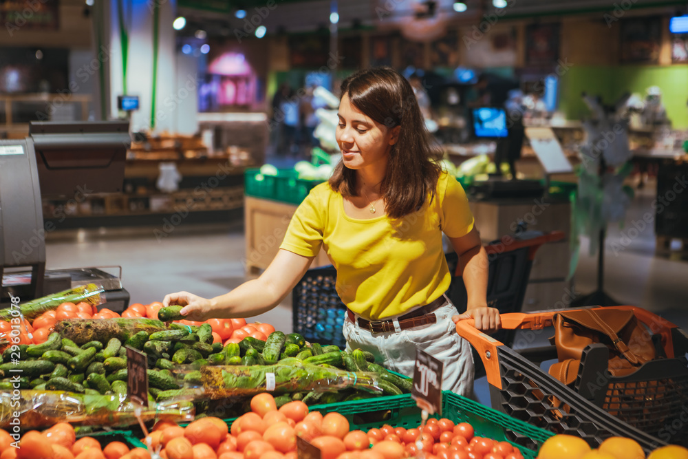 woman choosing cucumber from store shelf grocery shopping