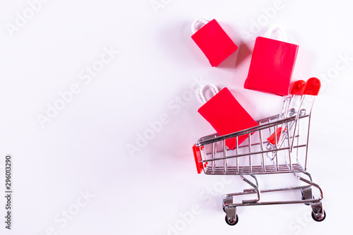 Trolley cart and red paper shopping bags on yellow background. Creative idea for shopping online, summer sale, supermarket, discount promotion and Black Friday concept. Copy space for text.