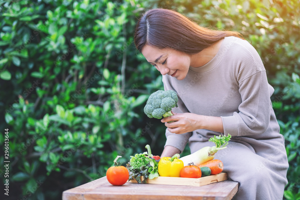 A beautiful woman picking and checking a fresh mixed vegetables from a wooden tray on the table