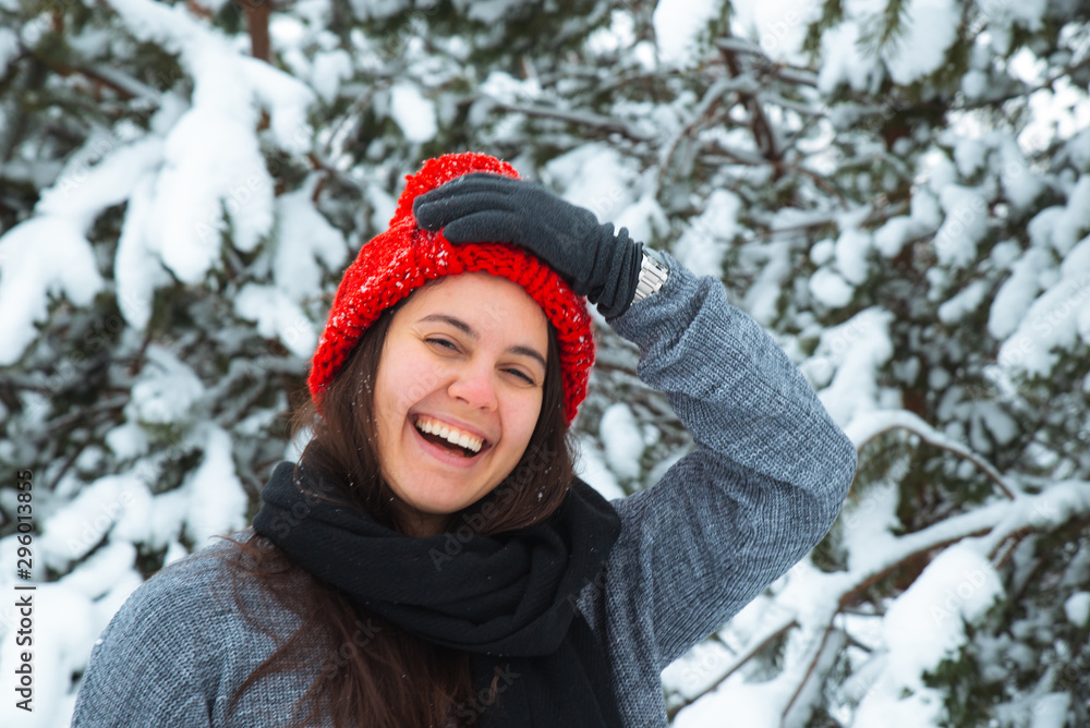 portrait of young smiling woman in winter clothes in red hat with bubo fir tree in background
