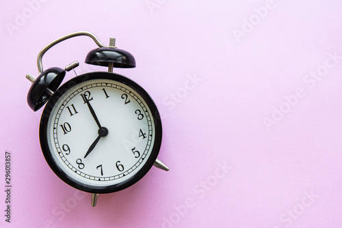 A black alarm clock isolated against pink background