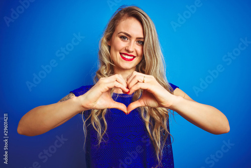 Young beautiful woman standing over blue isolated background smiling in love showing heart symbol and shape with hands. Romantic concept.