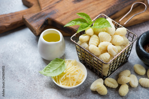 Raw potato gnocchi with green basil leaves, olive oil and grated parmesan over beige stone background