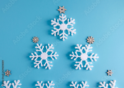 Christmas tree on a blue background from white snowflakes in the center of the background. Around are small wooden snowflakes and stars. Flat lay, top view.