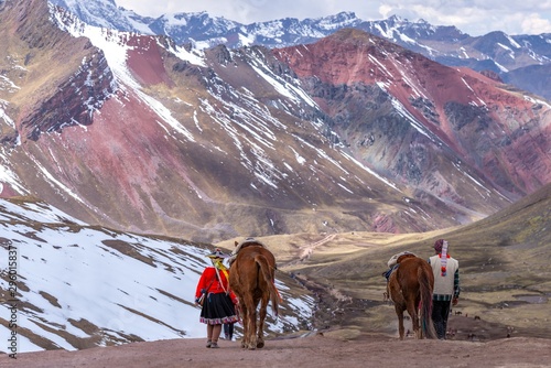 Horizontal shot of two persons in traditional Peruvian clothing walking on mountain with two horses