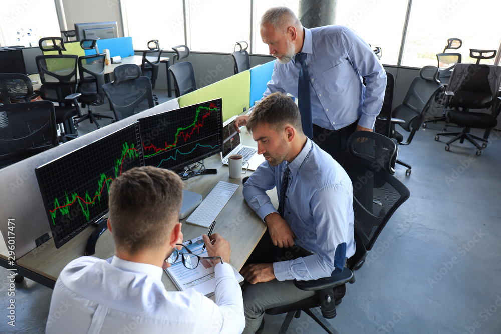 Group of modern business men in formalwear analyzing stock market data while working in the office. Group of modern business men in formalwear analyzing stock market data while working in the office.