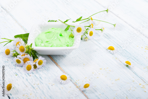 green cosmetis cream with chamomile flowers on white wooden table photo