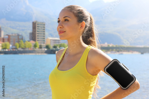 Successful positive female athlete wearing armband blank for advertising before running or exercising outdoor in summer. Woman success in sport lifestyle. photo