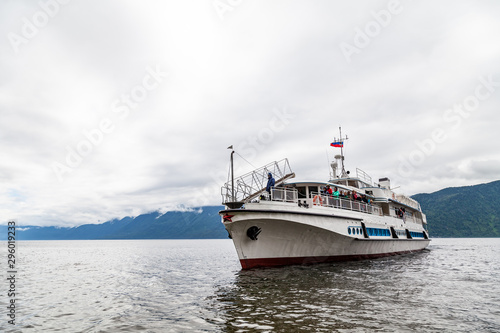 Large cruise ship during a walk on the water on the Teletskoye lake in the Altai mountains with tourists near the pier with rocks under the sky with clouds in the summer.