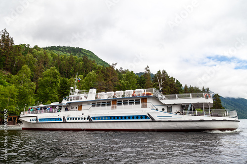 Large cruise ship during a walk on the water on the Teletskoye lake in the Altai mountains with tourists near the pier with rocks under the sky with clouds in the summer. © Aleksandr Kondratov