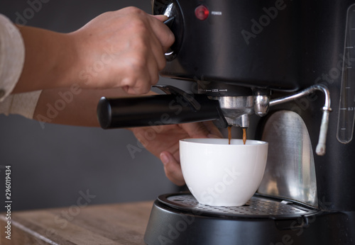 Woman hand making coffee with coffee machine on wooden counter.White cup for fresh hot coffee in the morning time at home.