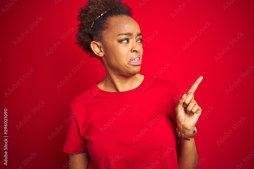 Young beautiful african american woman with afro hair over isolated red background Pointing aside worried and nervous with forefinger, concerned and surprised expression Young beautiful african american woman with afro hair over isolated red background Pointing aside worried and nervous with forefinger, concerned and surprised expression