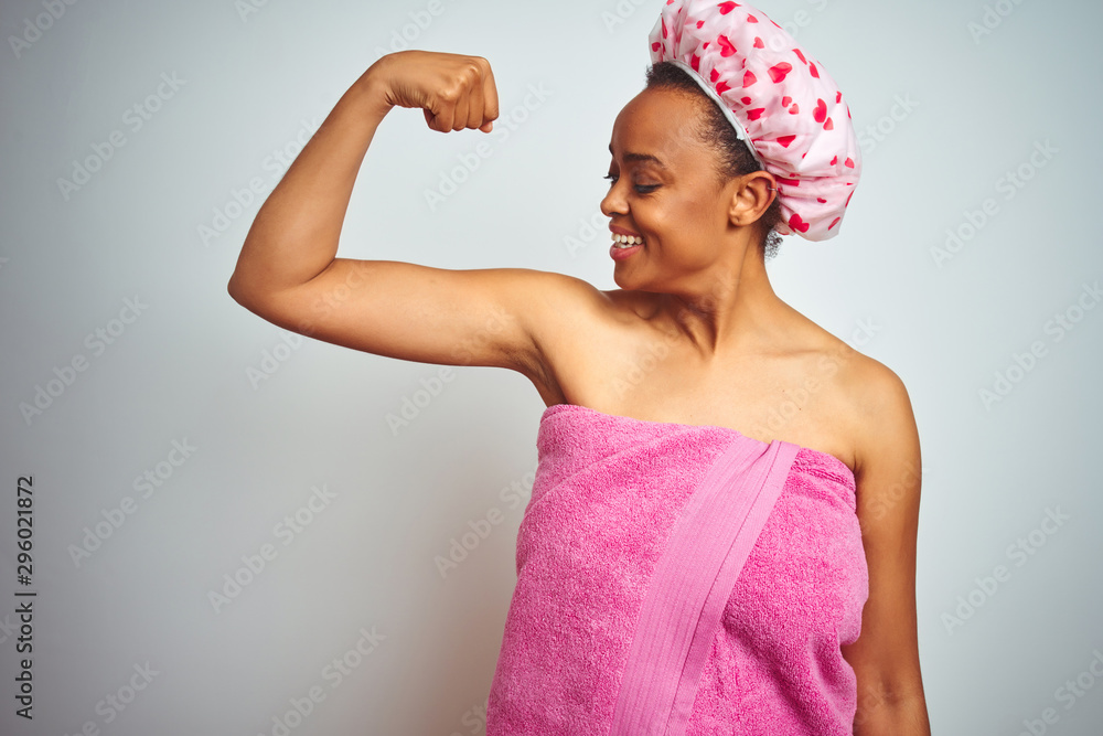 African american woman wearing pink shower towel after bath over isolated background showing arms muscles smiling proud. Fitness concept. African american woman wearing pink shower towel after bath over isolated background showing arms muscles smiling proud. Fitness concept.