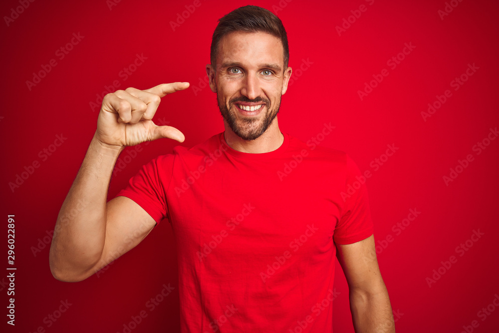 Young handsome man wearing casual t-shirt over red isolated background smiling and confident gesturing with hand doing small size sign with fingers looking and the camera. Measure concept. Young handsome man wearing casual t-shirt over red isolated background smiling and confident gesturing with hand doing small size sign with fingers looking and the camera. Measure concept.