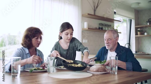 A small girl with senior grandparents indoors sitting at the table, eating. photo