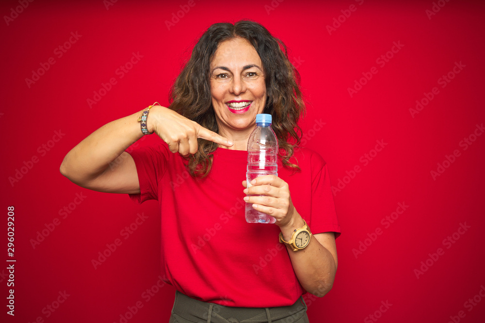 Middle age senior woman holding plastic water bottle over red isolated background very happy pointing with hand and finger Middle age senior woman holding plastic water bottle over red isolated background very happy pointing with hand and finger