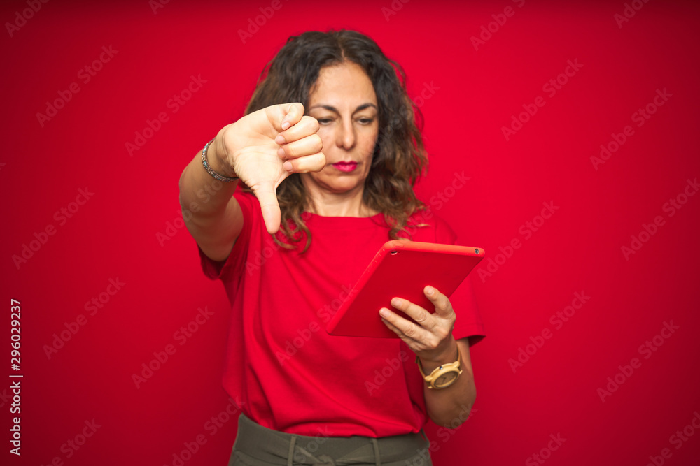 Naklejka premium Middle age senior woman using touchpad tablet over red isolated background with angry face, negative sign showing dislike with thumbs down, rejection concept