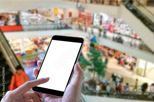 Mock up image of woman hand holding and using mobile smart phone with blank white scree in shopping mall center blur background.Mobile application,mobile banking,online shopping concept. Clipping path
