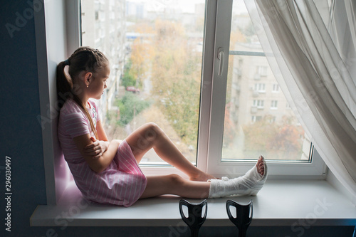 A teenage girl with a broken leg in a cast is sitting on a windowsill with crutches. Free Download A teenage girl with a broken leg in a cast is sitting on a windowsill with crutches. - GFXLoad
