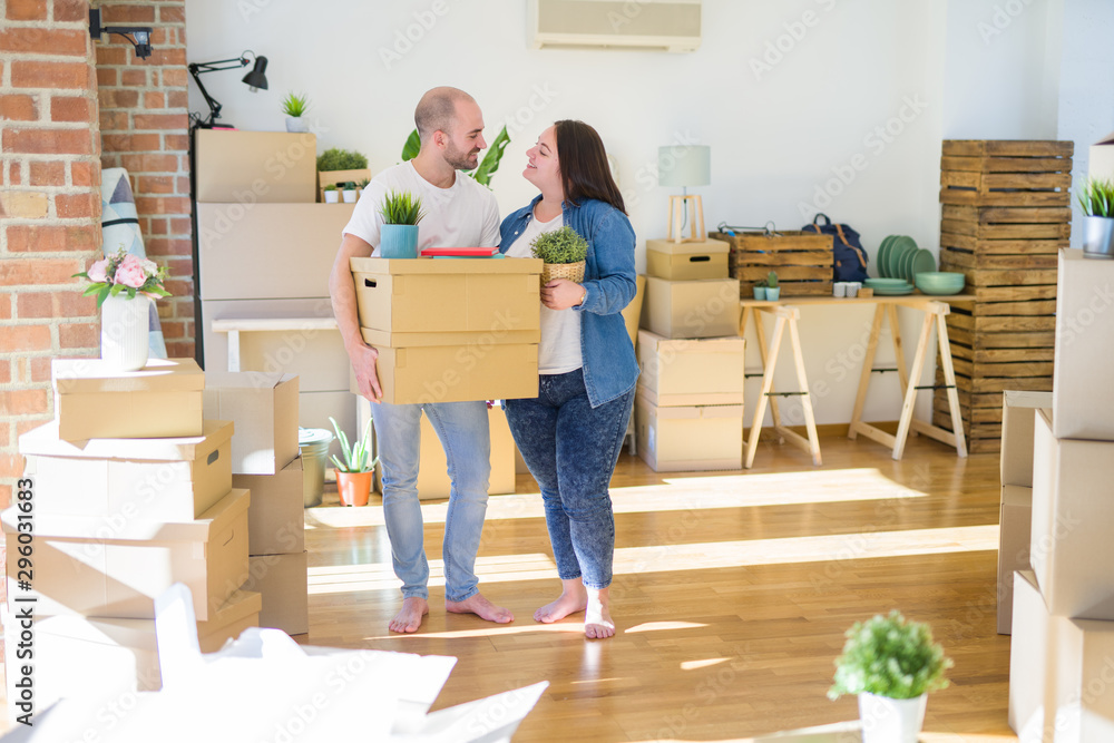 Young couple moving to a new home, smiling happy holding cardboard boxes - obrazy, fototapety, plakaty 
