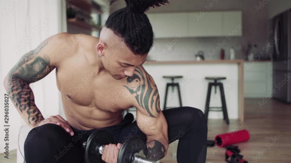 A young man doing exercise with dumbbells indoors at home, a body workout. A young man doing exercise with dumbbells indoors at home, a body workout.