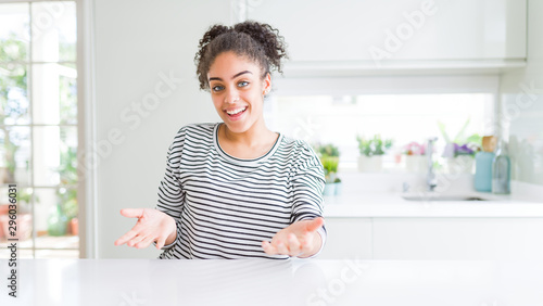 Beautiful african american woman with afro hair wearing casual striped sweater smiling cheerful with open arms as friendly welcome, positive and confident greetings