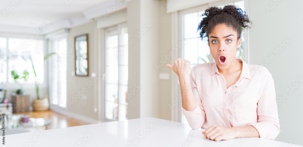 Wide angle of beautiful african american woman with afro hair Surprised pointing with hand finger to the side, open mouth amazed expression. Wide angle of beautiful african american woman with afro hair Surprised pointing with hand finger to the side, open mouth amazed expression.