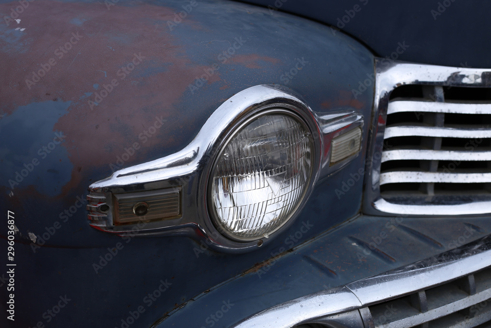 The headlight in the chrome trim of a retro American car in the original peeling blue coloring.