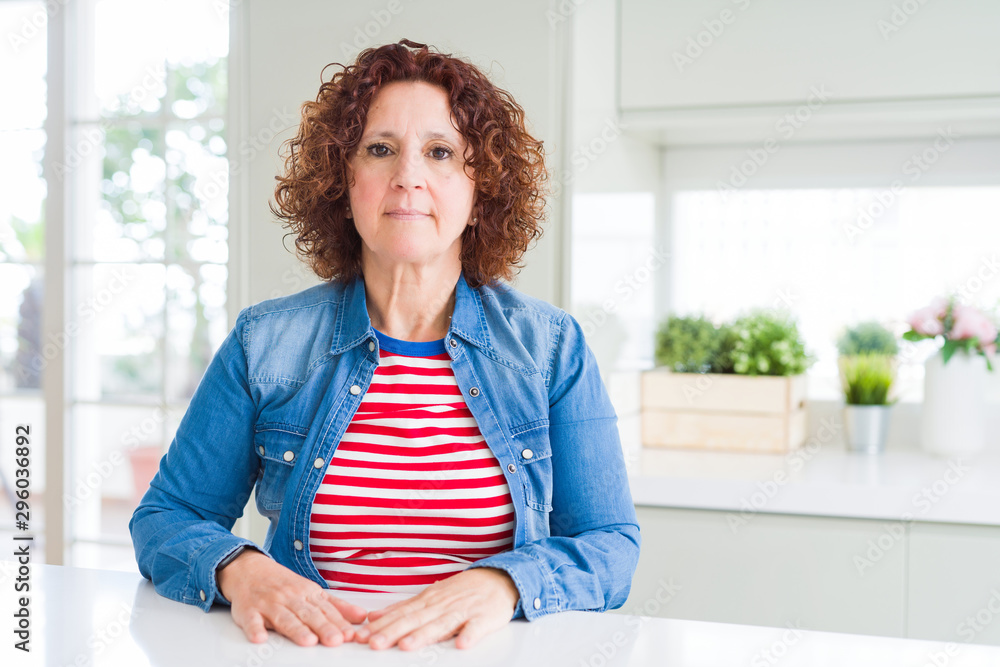 Middle age senior woman with curly hair wearing denim jacket at home Relaxed with serious expression on face. Simple and natural looking at the camera. Middle age senior woman with curly hair wearing denim jacket at home Relaxed with serious expression on face. Simple and natural looking at the camera.