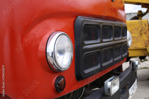 Side view of the front of an old red Soviet truck, round headlight and grille.